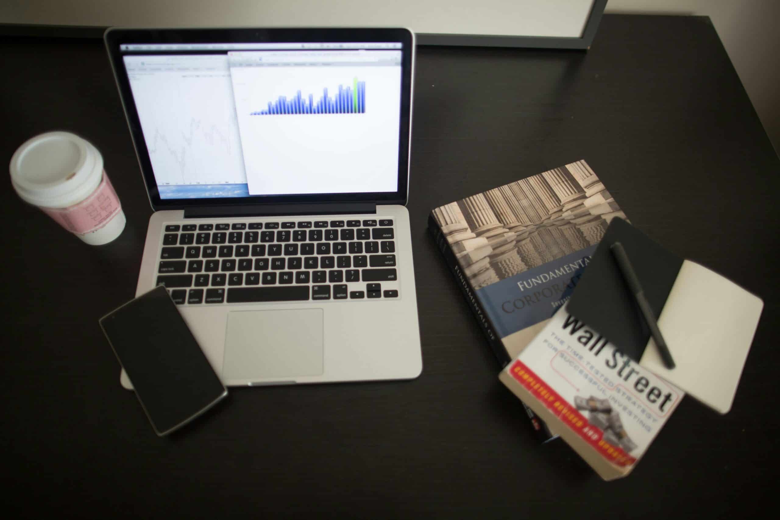 Apple Macbook next to a takeaway coffee, phone, and textbooks