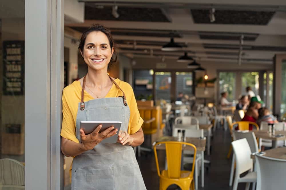 happy cafe owner standing in the doorway, smiling and holding a tablet